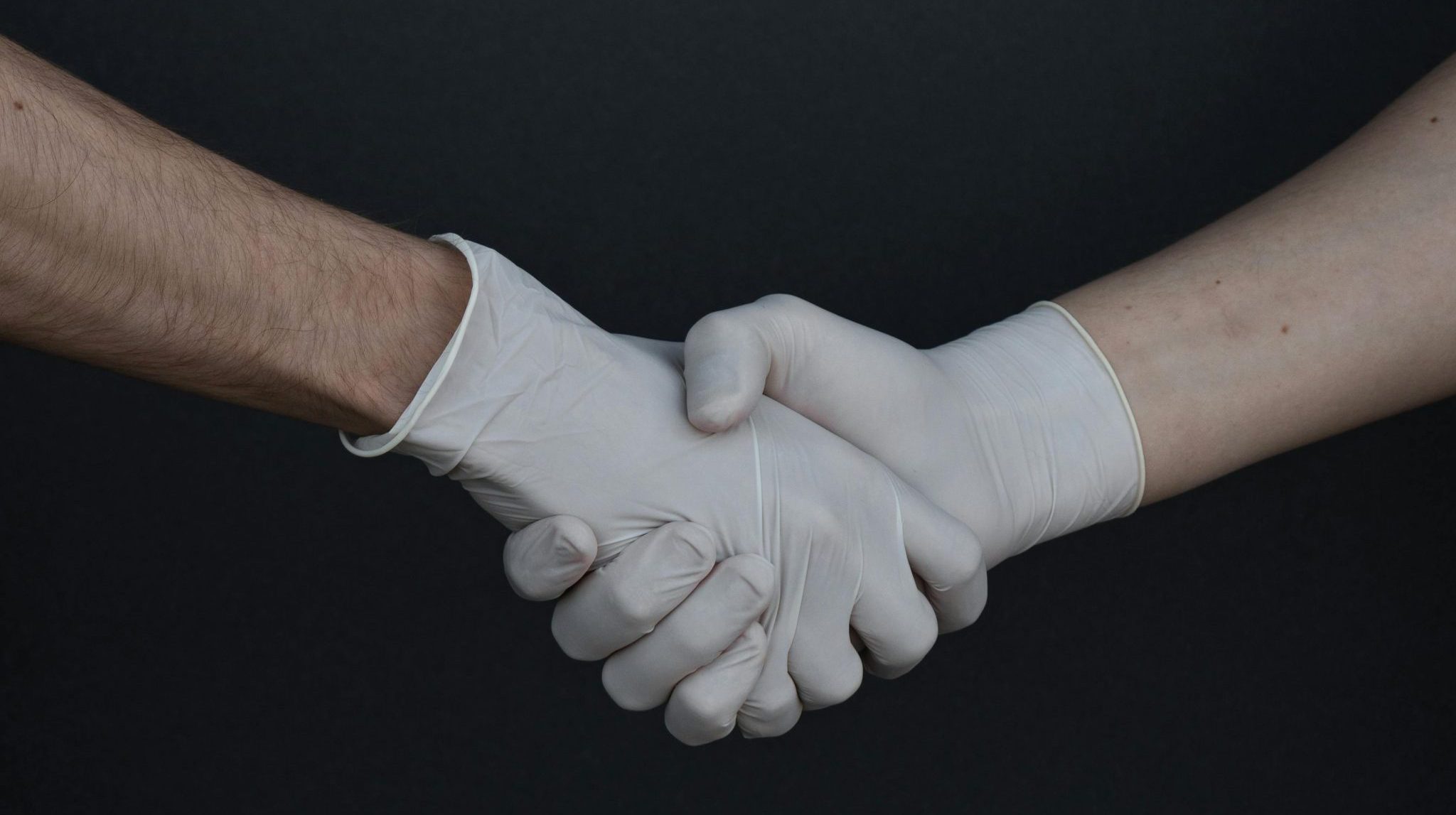 Two people shaking hands while wearing latex gloves, illustrating safety and protection.