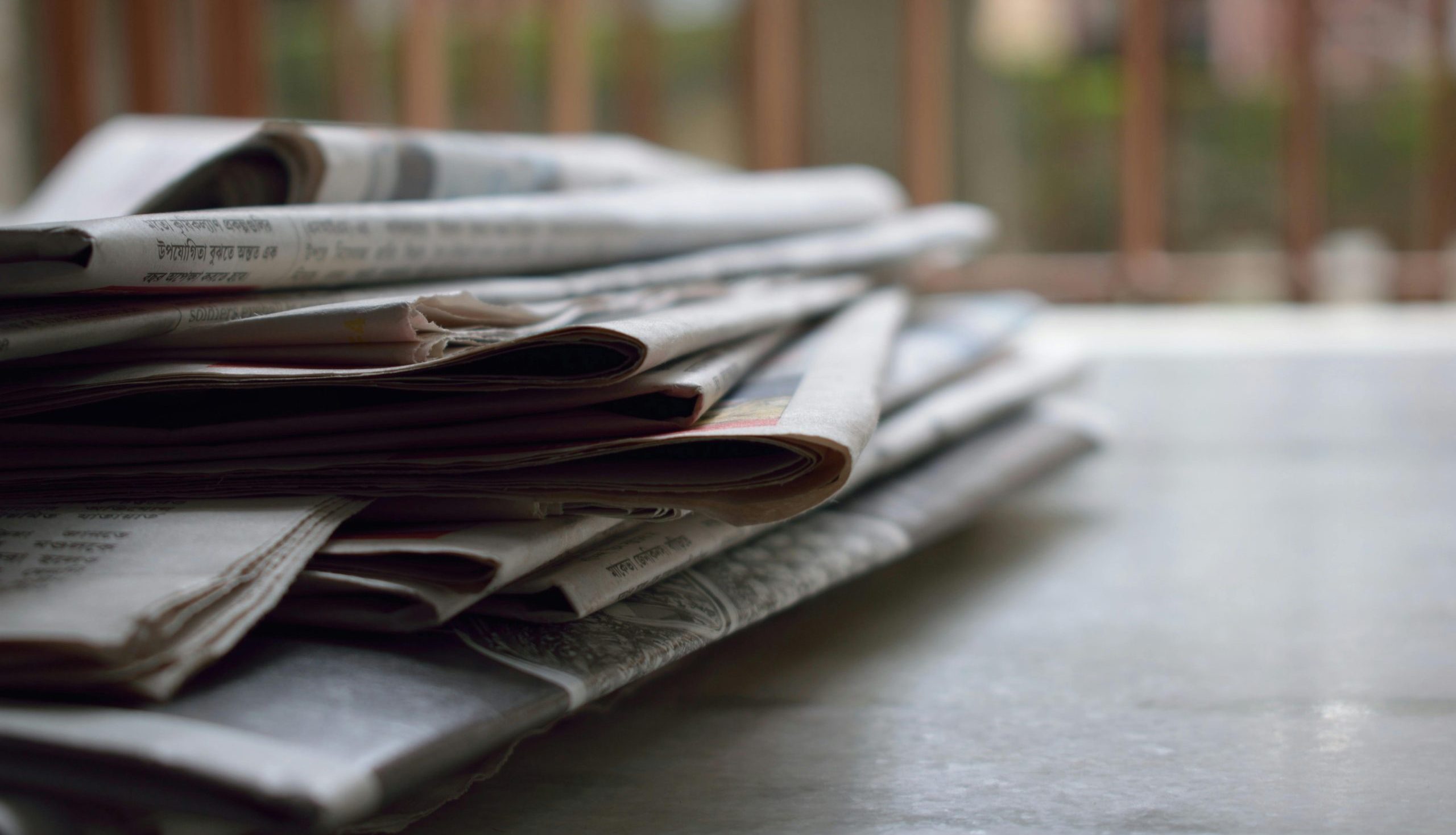 A close-up of a stack of newspapers resting on a desk, symbolizing information and media.